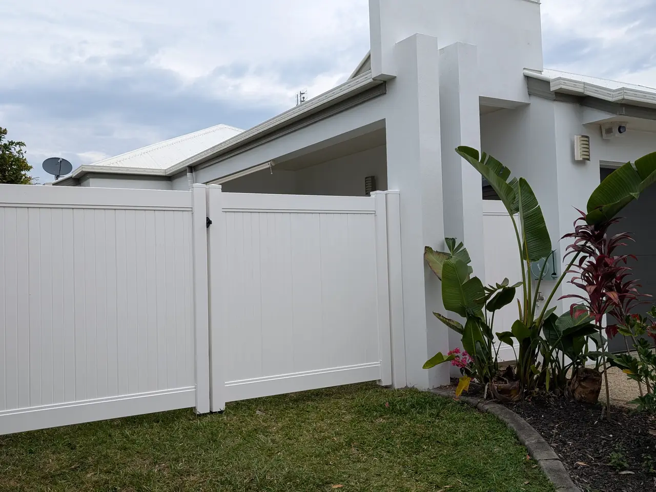 White PVC privacy fence and gate along the side of a modern home