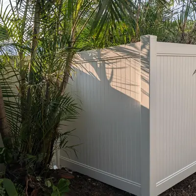 Tall white PVC privacy fence around a garden with palms