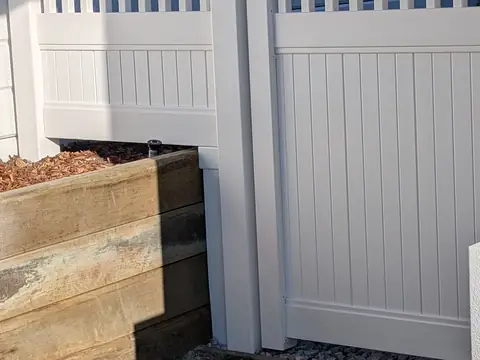 White PVC fence panel with slatted top section beside a garden bed